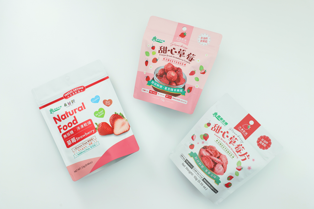 義美生機凍乾草莓果乾，甜心草莓、真甘純草莓、甜心草莓片的包裝袋平放在白色桌面上