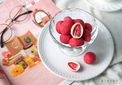 玻璃杯裡放了許多粒草莓巧克力，旁邊有白色陶瓷盤子、粉紅內頁的雜誌，眼鏡做裝飾。
