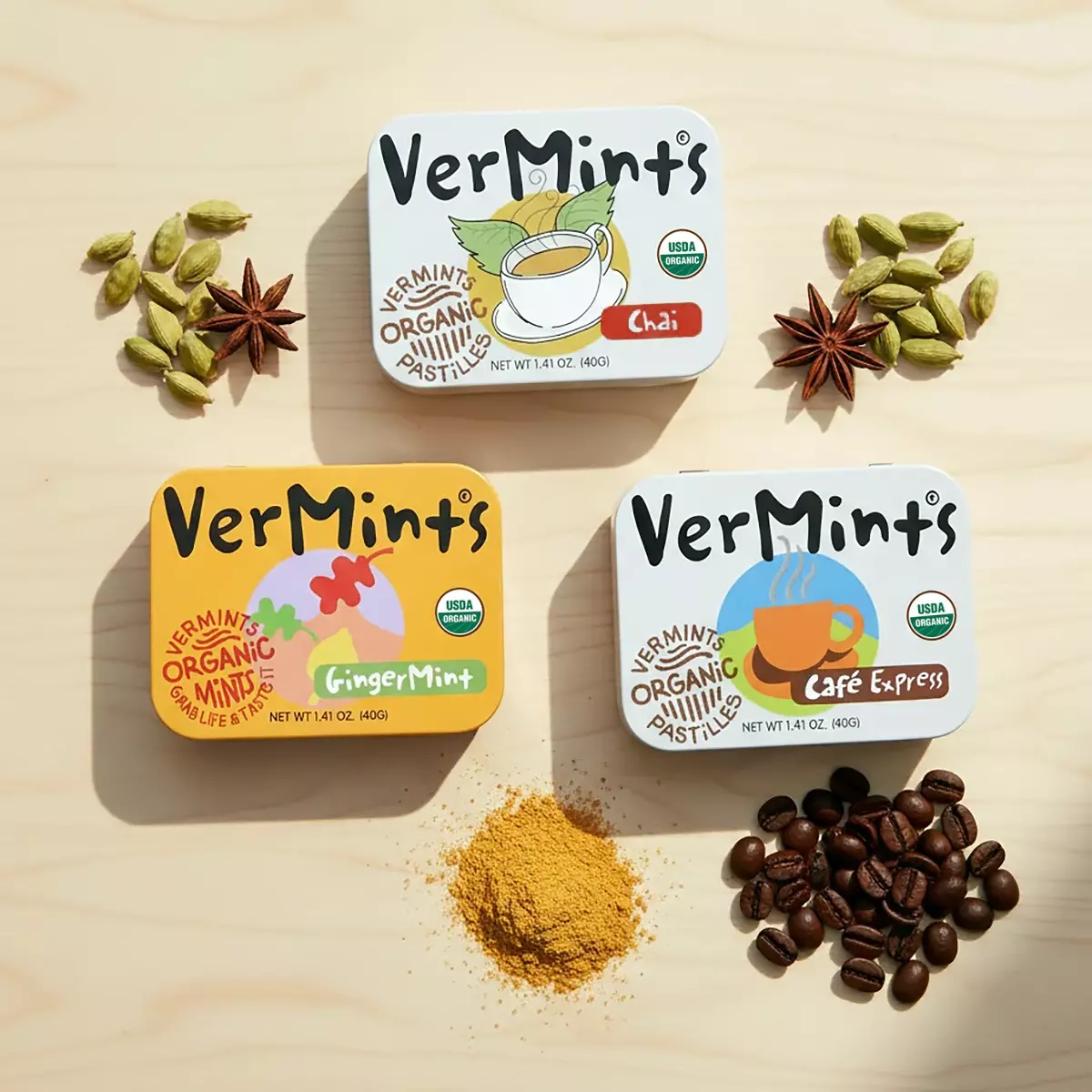 VerMints印度柴茶、咖啡、薑汁風味三款有機清口糖鐵盒放射排列，周邊散布咖啡豆、薑粉與香料。木質桌面溫暖自然光，美學生活獨特風味氛圍。
