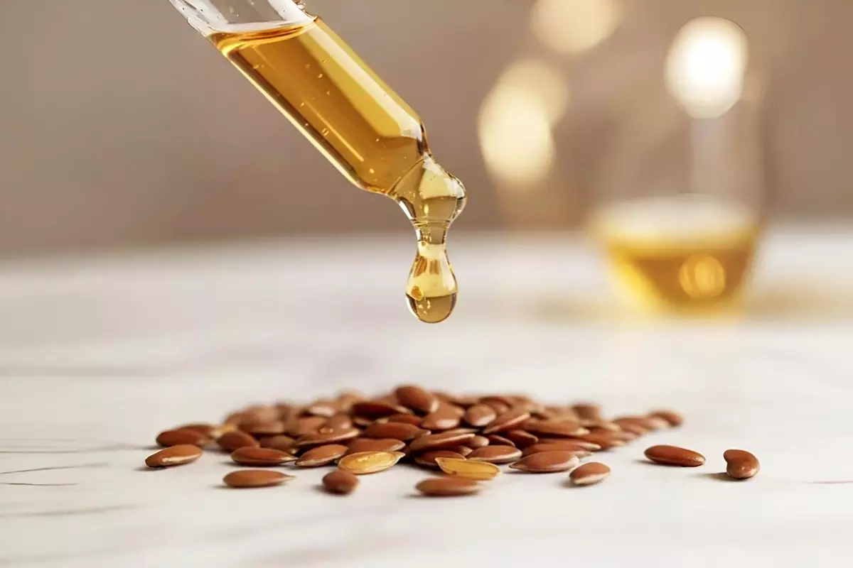 微距攝影捕捉單顆金黃透明亞麻仁油從玻璃滴管滴落，琥珀色澤折射柔光，白大理石面上環繞清晰亞麻籽。細膩紋理與柔和陰影。